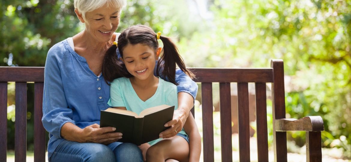 Smiling grandmother reading novel to granddaughter sitting on